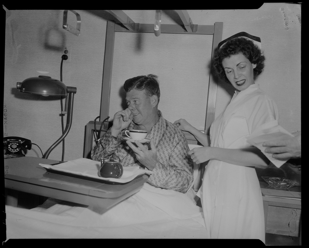 Arthur Godfrey holding tea cup with nurse looking on