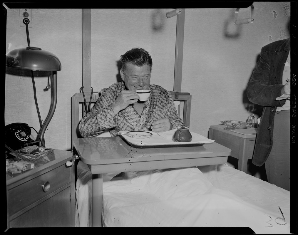 Arthur Godfrey in hospital bed, drinking from tea cup