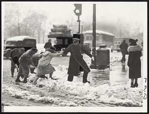 Crossing the Tremont Alps--This picture was taken today at the corner of Boylston and Tremont streets where, with the aid of a policeman, a woman is being literally shoveled over a snow bank as she crosses the street. Note the workman putting down a shovel for her to step on--the 20th century equivalent of the old Sir Walter Raleigh story.