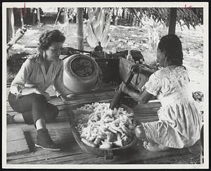 Betty Adams with Inca native watches as a Peruvian Indian woman in jungle village along Amazon makes an alcoholic beverage from Yucca root.