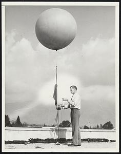 Balloons Radio Data from Stratosphere To Scientist. Pasadena, Calif. Balloons carrying weather recording and broadcasting apparatus are being flow to the stratosphere from atop the roof of the California Institute of Technology. Developed by Louvan E. Wood, the weather recorder continuously records air pressure, temperature and humidity which is, in turn, broadcast to a receiving set on the ground by a tiny transmitter also attached to the balloon. The equipment weighs about one pound. The balloon is flown to altitudes of 60,000 feet. It is hoped that the balloon apparatus will take the place of costly airplane weather testing flights now being used. PHOTO SHOWS: Louvan E. Wood, with the stratosphere robot balloon. Excluding the balloon and parachute, the weather instruments, which weigh together less than three ounces, include a minute aneroid barometer, a bi-metallic strip that serves as a thermometer, and a hair plucked from Wood's head that measures humidity. Moved by a special watch that ticks twenty times a second and forms a vital part of the balloon's cargo, a metal hand that serves as a watch hand rotates slowly. When the hand touches an arm attached to the barometer, a contact is made that broadcasts a signal. As air pressure decreases, the position of the barometer hand changes. This makes the pressure signal contacts father apart.