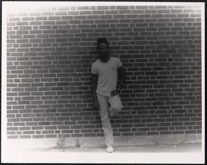 Young man posing with hand on hip against brick wall