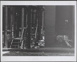Unidentified street, man sleeping on stoop