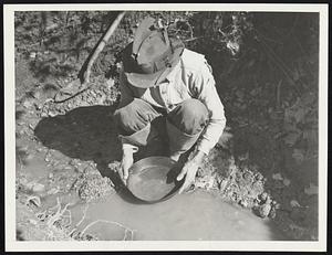 Washing Georgia Gold (1). In neither Alaska nor California but in Georgia, a half mile outside Dahlonega, was this picture made shown washing gold from a dam-controlled stream is William (Bill) Jenkins, 46-year-old World War Veteran, who operates on the Crown Mountain Mine Property. Jenkins gives the owner 10 per cent of the gross and acts as caretaker of the property. In No.2 (21148) is shown how mercury is "burned off" the gold.