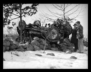 Spectators pose by an overturned car