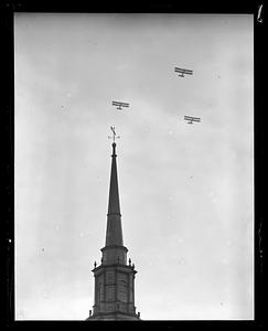 Three biplanes flying over a steeple