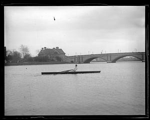 A man rowing a scull on the Charles, Larz Anderson Bridge and Weld Boathouse in background