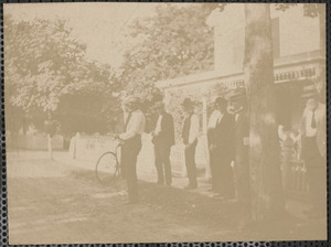 Six unidentified men standing by street with one holding bicycle