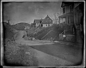 Unpaved road, fire hydrant, several residential buildings set on a hill