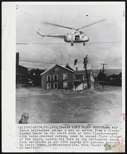 Air Lift Flood Rescue- An air Force helicopter swings a man to safety from a floodlashed house in the south side of this flood-ravaged city today. Another person, seen in second floor window of the house, awaits his turn as the helicopter swung back and forth to air lift nearly 100 persons trapped in their homes.