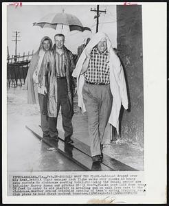 Bengals Walk the Plank-Raincoat draped over his head, Detroit Tiger Manager Jack Tighe walks over planks in heavy rain enroute to clubhouse meeting today. Following the Bengal mentor are infielder Harvey Kuenn and pitcher Billy Hoeft. Planks were laid down some. 75 feet in order to aid players in avoiding mud on walk from cars to the clubhouse. Weather erased scheduled opening of team's spring training camp Club plans to hold first workout tomorrow.