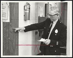 Stow Police Chief Winthrop Addy points to bullet hole in wall at Purity Foods supermarket following gunfight.