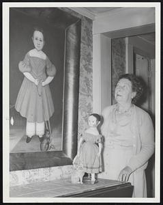 Isaniah Walker doll stand on table in front of painting that could be a copy of itself. At right is Mrs. Norman B. Hunt.