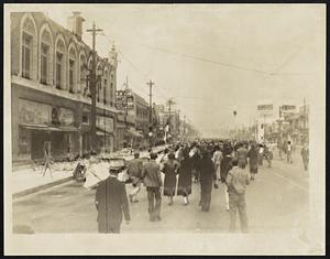 Huntington Park, After The Earthquake. A street scene in the Huntington Park district of Los Angeles the day after the earthquake, showing people walking in the center of the street to avoid possible falling bricks. Twelve people were killed in this district. At left is the damaged elks club. This picture was telephotoed from Los Angeles to New York.