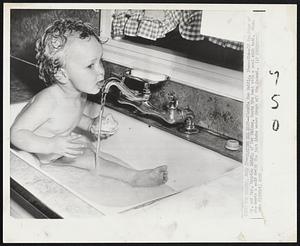 Beating the Heat-Claudia Sue Neidig, 16-months-old daughter of Mr. and Mrs. Maurice Neidig of Des Moines, beats the heat with a cool sink bath. When she wants a cold drink she just licks water drops off the faucet.