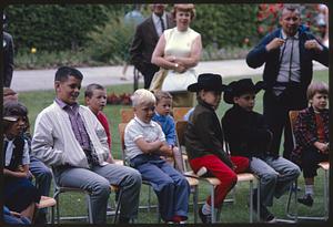 Adults standing behind row of children watching puppet show, British Columbia