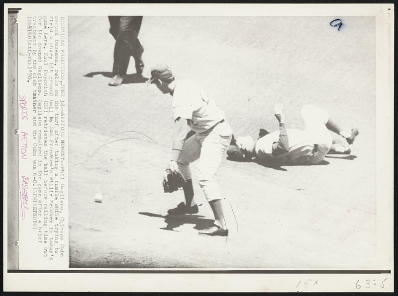 Anxious Moments -- Phil Gagliano, Chicago Cubs second baseman, rolls on the turf after taking a tumble while trying to field a sharp hit ground ball by San Francisco's Willie McCovey in today's game here. Paul Popovich (22) retrieves the ball before calling time out for the downed Gagliano. Gagliano remained in the game after a brief treatment by the club trainer and the Cubs won 6-0.