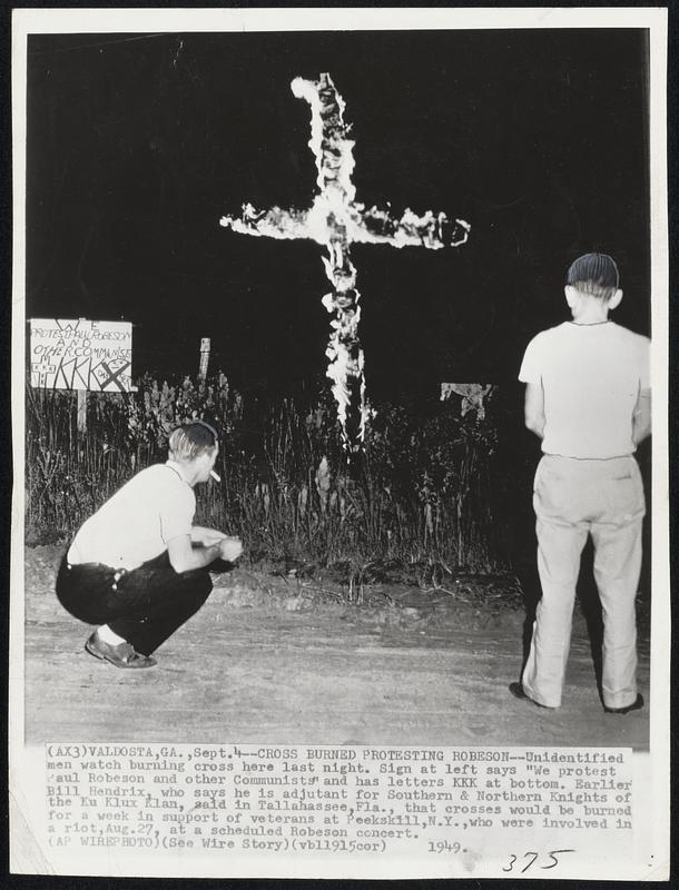 Cross Burning Protesting Robeson--Unidentified men watch burning cross here last night. Sign at left says “We protest Paul Robeson and other Communists” and has letters KKK at bottom. Earlier Bill Hendrix, who says he is adjutant for Southern & Northern Knights of the Ku Klux Klan, said in Tallahassee,Fla., that crosses would be burned for a week in support of veterans at Peekshill,N.Y.,who were involved in a riot,Aug.27, at a scheduled Robeson concert.