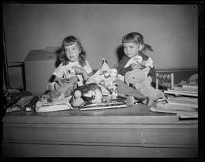 Two young girls with stuffed animals, dolls, and other toys