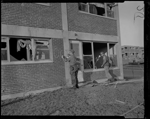 Military personnel, possibly from the American Red Cross, writing "OK" on brick wall of damaged building