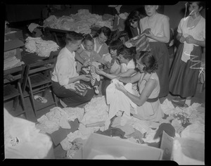 Group of people sorting through piles of clothes, checking if they will fit a young child