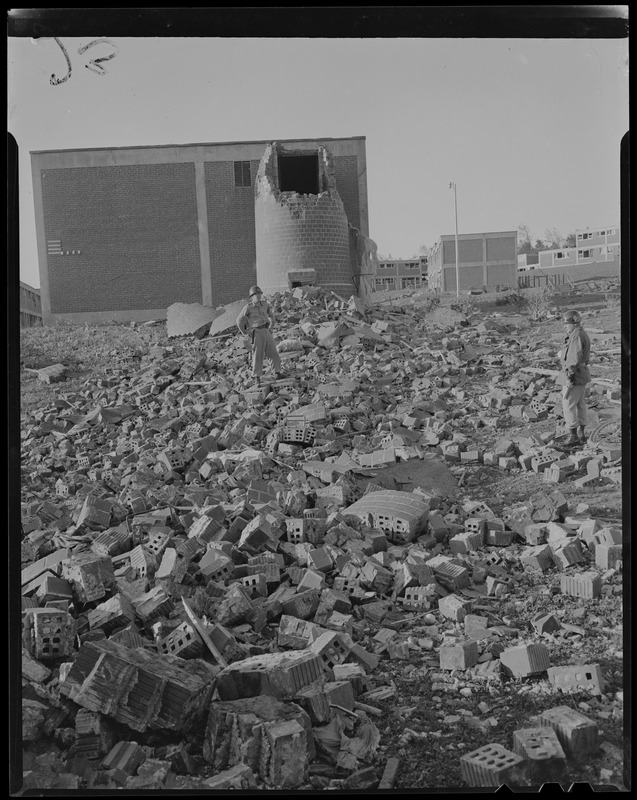 Military personnel standing on pile of rubble and debris left by tornado