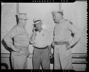 Police officer on telephone call, flanked by two military men