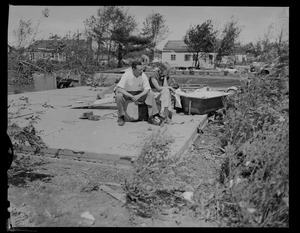 Man and woman sitting and looking at foundation of house and other wreckage caused by tornado, including a bathtub