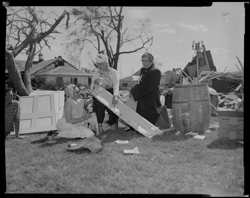 Four people sitting and talking amid wreckage, with a dog