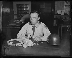 Military man seated at desk, examining found jewelry and other items
