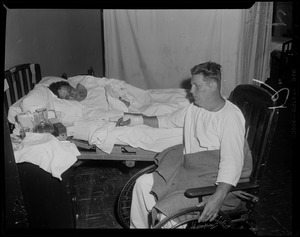 Man with bandaged hand seated in wheelchair next to woman lying in bed