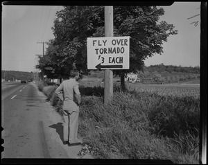Man standing on road next to sign reading "Fly Over Tornado $3 Each"