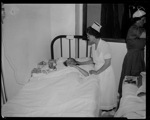 Nurse attending to patient in bed with another nurse nearby