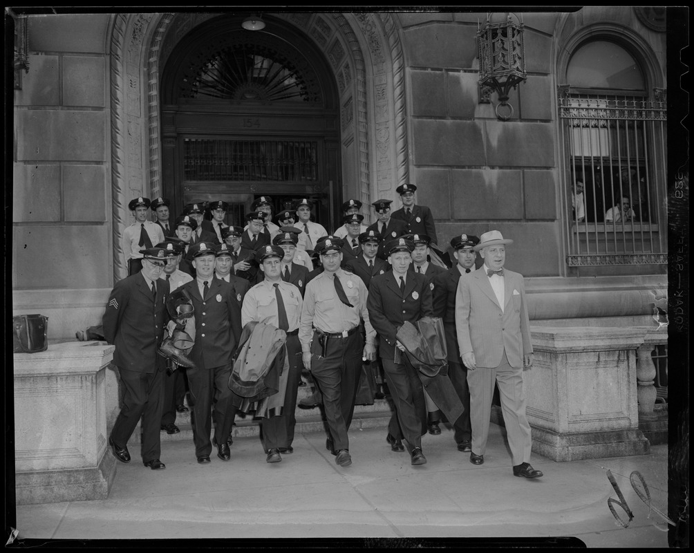 Uniformed police officers and man in suit walking out of Boston Police Department headquarters