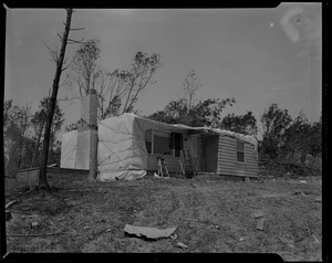 House damaged by tornado, partially covered with a tarp and surrounded by debris