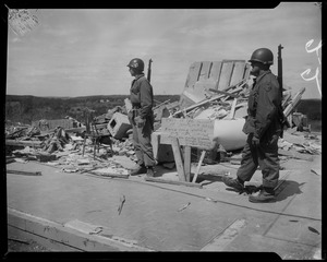 Two military men standing near tornado wreckage and a sign reading "This is the property of Malcolm Hanna"