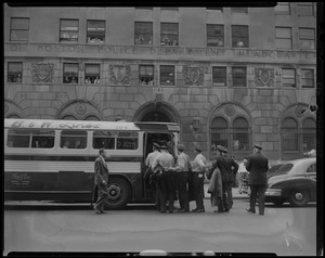 Uniformed police officers boarding a bus outside of Boston Police Department headquarters, with onlookers