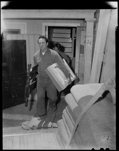 Man carrying box and headboard from bed out of a building