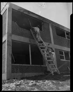 Man on ladder looking at second floor of building damaged by tornado