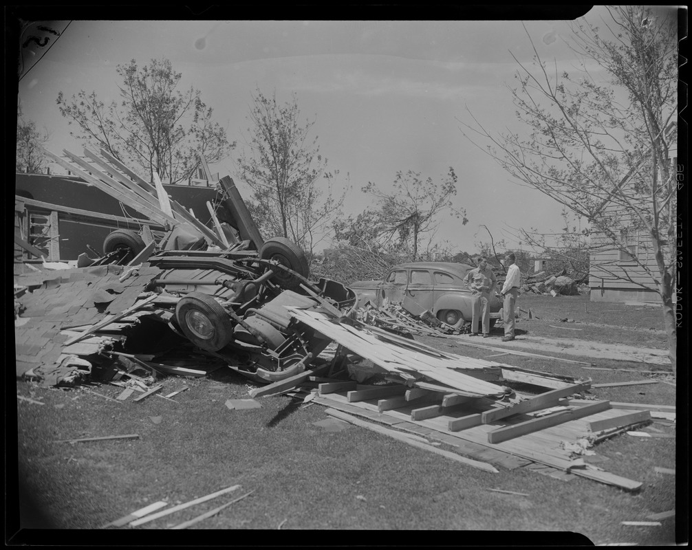 Two men standing near overturned car and other debris from tornado