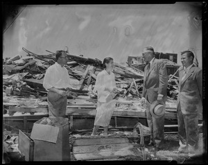 Man and woman talking to two men in suits amid wreckage from tornado