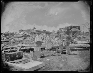 Man and woman talking to two men in suits amid wreckage from tornado