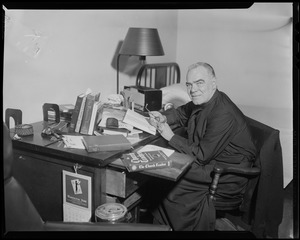 Fr. Joseph T. O'Callahan seated at desk, holding glasses