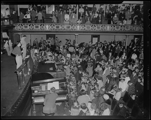 Man on stage at microphone with pianist, organist, and audience in front of him during revival service with Billy Graham