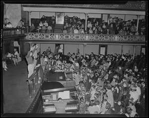 Man on stage at microphone with pianist, organist, and audience in front of him during revival service with Billy Graham