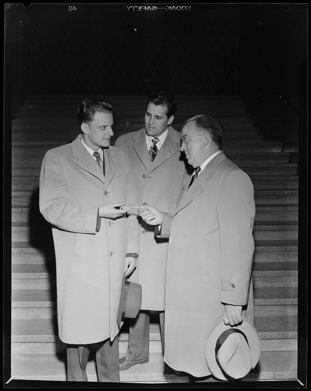 Billy Graham, left, in conversation with two men and holding a ...