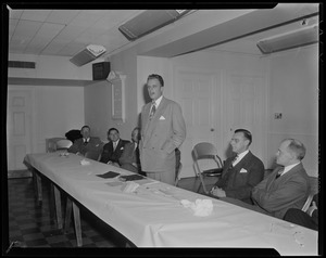 Billy Graham addressing room while other men seated at table look on
