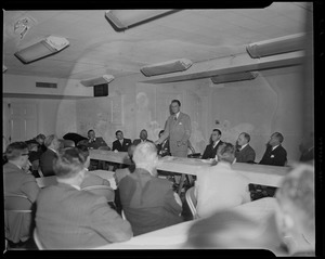 Billy Graham standing behind table, addressing the room