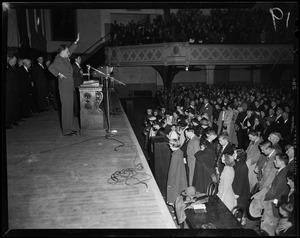 Billy Graham standing on stage behind podium and microphones in front of a crowd