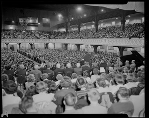 Audience seated at revival service with Billy Graham in Mechanics Hall, listening to man at podium, as seen from the stage